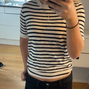 T-shirt  - Stickad T-shirt med ränder. En liten defekt som sytts längs ned på tröjan. Syns väldigt lite.