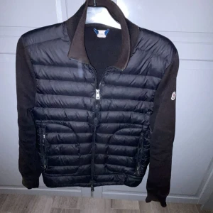 Svart cardigan från Moncler storlek S - Säljer en svart cardigan från moncler. Tyvärr lite trasig och solblek(syns på bild). Alla taggar funkar samt skanning. Säljer eller byter mot någon annan jacka. Hojta till om de är något finns fler bilder på jackan