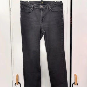 Svarta Lee Marion Straight jeans W32 L31 - Snygga svarta jeans från Lee i modellen Marion Straight. Klassisk femficksdesign, raka ben och normal passform. Jeansen är tillverkade i bomull med en liten mängd stretch för extra komfort. Perfekta till en avslappnad och stilren look.