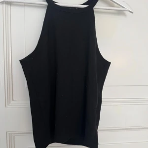 Svart ribbad linnetopp från BikBok - Säljer en svart ribbad linnetopp från BikBok i storlek M. Toppen har hög halsringning och är ärmlös med smala axelband. Perfekt för en clean och stilren look, lätt att matcha med olika outfits.