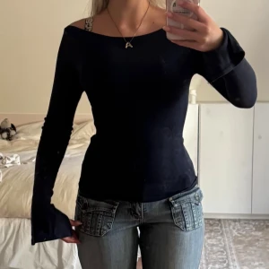Svart långärmad topp med utsvängda ärmar - Säljer en marinblå långärmad tröja med utsvängda ärmar, något offshoulder ringning. Toppen är figurnära och har en stilren look som passar perfekt till jeans eller kjol. Materialet känns mjukt och stretchigt, vilket gör den bekväm att bära.
