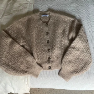 Beige stickad kofta från Adoore - Supermysig beige stickad kofta från Adoore med stora knappar framtill. Koftan har ballongärmar och ribbade muddar, perfekt för lager-på-lager. Använd endast en gång. Säljer billigare pga att den fortfarande finns på deras hemsida i stl 34. Nypris: 1700kr 