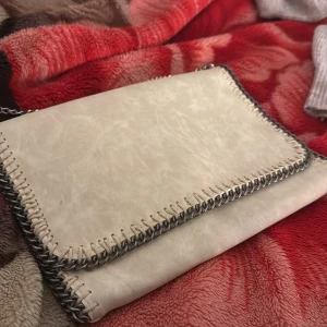 Beige axelväska med kedja - En vanlig plattväska i beige färg men har en liten fläck bakom den. Har inte använt den nån gång