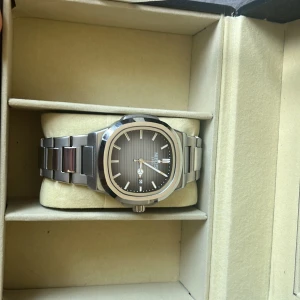 Silverfärgad Nibosi herrklocka - Stilren herrklocka från Nibosi med silverfärgat armband i metall och ljus blå urtavla med diskreta ränder. Urtavlan har datumvisning och minimalistiska markeringar. Klockan har en modern, rundad fyrkantig form och passar perfekt till dig som gillar cleana accessoarer.