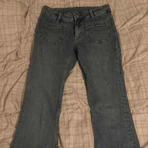 Blå bootcut jeans från 157 - Snygga blå jeans från 157 med klassisk bootcut-passform och raka ben. Jeansen har fem fickor, bälteshällor och en knappstängning fram. Materialet är slitstarkt denim och färgen är en tvättad blå ton som passar till det mesta. Storlek XS Short Length