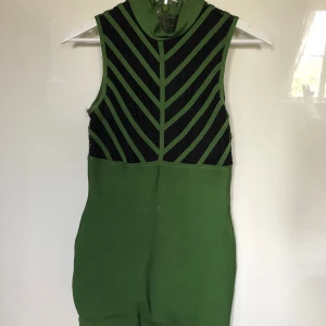 Grön och svart ärmlös kortklänning - Snygg grön och svart ärmlös kortklänning med grafiskt mönster upptill och markerad midja. Klänningen har dragkedja bak och är tillverkad i ett stretchigt material som sitter tight. Perfekt för dig som vill sticka ut med en cool look. 