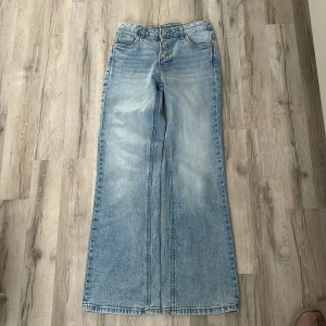 Ljusblå jeans med knappar - Snygga ljusblå jeans med breda ben och hög midja. Klassisk femficksmodell med synliga silverfärgade knappar framtill och orange kontrastsömmar. Jeansen har en avslappnad, trendig passform och är tillverkade i denim.