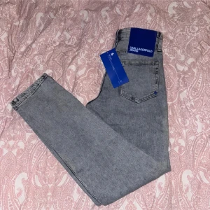 Grå slim jeans från Karl Lagerfeld - Snygga grå jeans från Karl Lagerfeld Jeans i slim fit-modell. Jeansen har stretchigt denimtyg för extra komfort och sitter under midjan. Klassisk femficksdesign och diskret logga på bakfickan. Perfekta för en clean och stilren look.