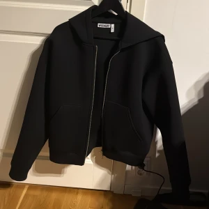 Svart hoodie med dragkedja från Weekday - Svart hoodie från Weekday i storlek M. Tröjan har dragkedja framtill, två stora fickor och en rejäl huva. Oversized passform med långa ärmar, perfekt för en chill och stilren look. Aldrig använd!
