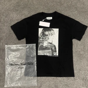 Maison Margiela svart t-shirt med print - Svart t-shirt från Maison Margiela med coolt grafiskt print i vitt framtill. Klassisk rund hals och korta ärmar. T-shirten är gjord i mjuk bomull och har Margielas signaturdetaljer i nacken. Perfekt för dig som gillar streetwear med edge.
