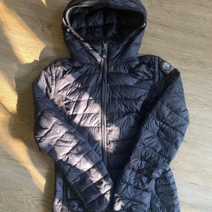 Mörkblå lättviktsdunjacka Parajumpers - Mörkblå lättviktsdunjacka från Parajumpers med huva och broderad logga på ärmen. ”Lufthål” i armhålorna på båda sidorna (se bild 4). Den är väldigt fin och har inga tydliga tecken på användning. Dock så har den fått lite missfärgning vid ”informationslappen” (se bild 4). Har verkligen älskat denna jackan! Såklart äkta! 
