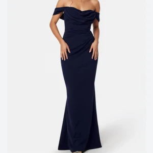 Marinblå offshoulder långklänning - Säljer en marinblå långklänning med offshoulder och draperad överdel. Klänningen har figurnära passform och markerad midja, vilket ger en elegant siluett. Perfekt för bal eller andra speciella tillfällen. Materialet är mjukt och följsamt. Endast använd en gång. 