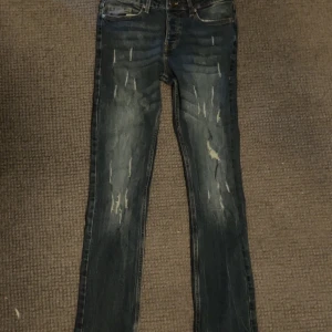 X blå slitna jeans W29 L32 - Säljer ett par blå jeans med slitna detaljer och snyggt tvättad look. Jeansen har klassisk femficksmodell, raka ben och orangea sömmar. Märkespatch bak i midjan och metallknappar framtill. Sitter i slim