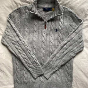 Kabelstickad grå Ralph Lauren halfzip - En galet snygg halfzip från RL, kabelstickad med krage och dragkedja. Nytt skick, strl M, värmer bra och levererar elegant stil på samma gång.                                  ⚜️Få ett GRATIS armband vid köp av detta plagg.     Välj mellan ett Anchor eller cuff armband, annars medföljer ett slumpmässigt utav de två⚜️