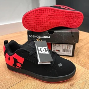 Svarta DC sneakers med röd logga - Snygga svarta DC sneakers med stor röd DC-logga på sidan och röd sula. Skorna levereras med originalkartong. Helt nya, aldrig använd.