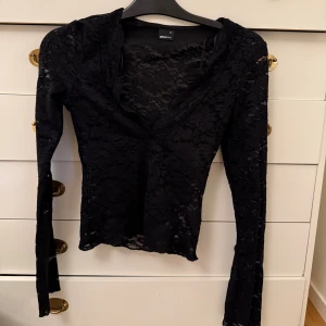 Svart spetsblus från Gina Tricot - Säljer en svart långärmad blus från Gina Tricot i transparent spets med blommigt mönster. Toppen har v-ringning och sitter tight. Perfekt för dig som vill ha en snygg och stilren look med lite edge.