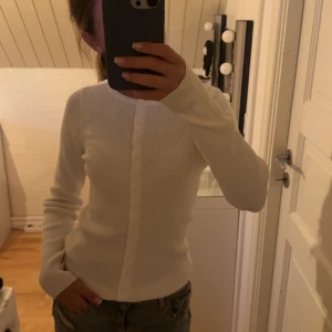 Vit ribbad kofta från 157, stl S - Säljer en vit ribbad kofta från 157 i storlek S. Koftan har långa ärmar, rund halsringning och knäppning framtill med små vita knappar. 