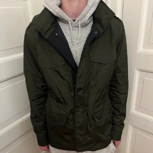 Field jacket - Field jacket från märket Hugo Boss, storlek 48 och är lite stor för mig som är 180 cm, super bra skick, justerbar i midjan och innerfickor finns, färgen inuti jackan är mörkblå och där med luvan som går att ta ut, jackan är ganska tunn så passar perfekt med väst under, skriv vid frågor!