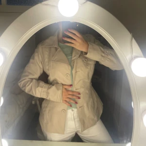 Beige trenchcoat med bälte only - Snygg beige trenchcoat med markerad midja och knytskärp i ryggen. Jackan har stora slag, knappar framtill och långa ärmar. Perfekt för dig som vill ha en klassisk och stilren look. Passformen är normal och materialet känns som bomull.