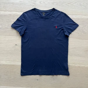 Marinblå t-shirt från Polo Ralph Lauren - Snygg marinblå t-shirt från Polo Ralph Lauren med klassisk röd broderad logga på bröstet. Modellen är custom fit och har rund halsringning och korta ärmar.