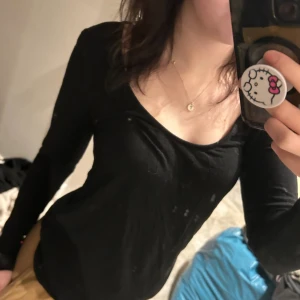 Svart långärmad tröja  - En svart långärmad topp med djup u-ringning. Modellen är enkel och tight, perfekt att styla med jeans eller kjol. Tunt och mjukt material. Storlek L.🌻 (smutsig spegel🫣)