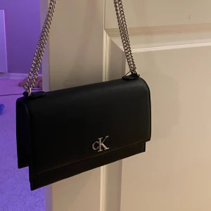 Ny💕 calvin klein - Nypris 1400kr! Snygg svart axelväska från Calvin Klein i stilren design med silverfärgad kedja och CK-logga framtill. Perfekt storlek för det viktigaste och passar till många outfits. Aldrig använd.❤️tryck gärna på ”köp direkt” säljer då jag behöver pengar