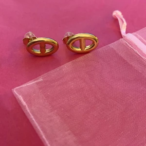 Guldiga ovala örhängen - Snygga små örhängen i guldigt metall med oval form och en stilren design. De har en öppen mittdel och stift med transparenta pluppar. Perfekta för dig som gillar minimalistiska smycken med en modern touch.