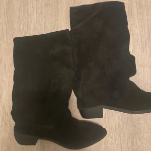 Svarta mockastövlar med låg klack - Säljer ett par svarta stövlar i mocka med låg klack och rund tå. De har en klassisk och enkel design som passar till många olika outfits. Perfekta för höst och vinter när du vill ha både stil och komfort.