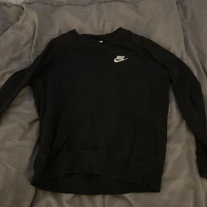Svart Nike sweatshirt i bomull - Svart sweatshirt från Nike med klassisk vit logga på bröstet. Tröjan har rund halsringning och långa ärmar, perfekt för en chill och sportig look. Tillverkad i mjuk bomull som känns skön mot huden.