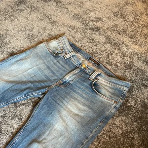 Ljusblå jeans från Nudie Jeans - Säljer ett par ljusblå jeans från Nudie Jeans med klassisk femficksdesign. Jeansen har raka ben och orangea sömmar, samt Nudie-logga på bakfickorna. Jeansen har ett hål under men syns inte på bilderna så fråga om bild om ni vill se det!Perfekta för dig som gillar en avslappnad och stilren look.