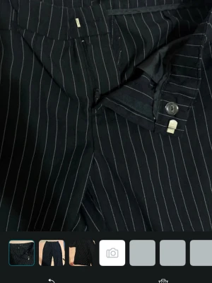 Svarta kostymbyxor med vita ränder - Snygga svarta kostymbyxor från Gina Tricot med tunna vita kritstrecksränder. Byxorna har raka ben, hällor för skärp och klassisk knapp- och dragkedjestängning. Perfekta för en stilren och trendig look.