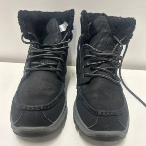 Svarta vinterkängor från HH HELLY HANSEN med foder 43 - Snygga svarta kängor från HH HELLY HANSEN med grov sula och snörning. Insidan är fodrad med mjukt material för extra värme. Ovandelen är i slitstarkt syntetmaterial och detaljer i textil. Perfekta för kalla dagar och ger en cool streetwear-look.