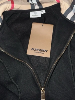 Svart Burberry zip up hoodie - Säljer fin oanvänd svart burberry tröja i storlek L men den passa då M också.
