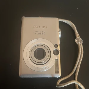 Canon Digital IXUS 60 kompaktkamera - Snygg och smidig silverfärgad Canon Digital IXUS 60 kompaktkamera med 6.0 megapixlar och Canon Zoom Lens 3x optisk zoom. Kameran har en stor display på baksidan och tydliga knappar för enkel navigering. Metallhölje och handledsrem ingår.laddare finns ej !