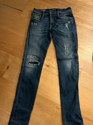 Replay Anbass med slitningar - Säljer ett par blå jeans från Replay med snygga slitningar och hål på benen. Jeansen har klassisk femficksmodell, normal midja och raka ben. Storleken är W29 L32! Priset kan diskuteras!