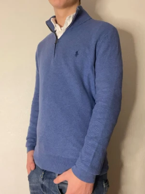 Blå quarter-zip från Ralph lauren - Snygg blå tröja från Ralph Lauren med 1/4 dragkedja och diskret logga på bröstet. Tröjan har ribbade muddar vid ärmslut och nederkant samt en klassisk passform. Jag är 178 och den passar perfekt skulle jag säga!