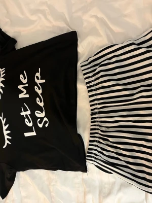 Svart pyjamas med text och randiga shorts - Pyjamas-set med svart t-shirt med trycket 'Let Me Sleep' och vita ögonfransar. Tillhörande shorts i svartvitt randigt mönster med resår i midjan och volanger längst ner. Mjukt och bekvämt material. Storlek 150 men passar XS!🤍