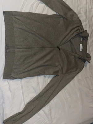 Grå ziptröja från Selected Homme - Stilren grå ziptröja från Selected Homme med hel dragkedja framtill. Tröjan har långa ärmar, ribbade muddar och är tillverkad i mjukt, tunt material som passar perfekt för lager på lager. Enkel och clean design utan mönster.