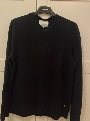 Svart tröja från Jack & Jones Core - En stilren svart tröja från Jack & Jones Core med rund halsringning och lång ärm. Tröjan har en enkel design och en liten gul detalj nertill. Perfekt för en clean och klassisk look.