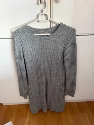 Grå kabelstickad klänning - Mysig grå stickad klänning med kabelstickat mönster längs axlarna och ribbstickad struktur. Är i storlek xs men passar S. 