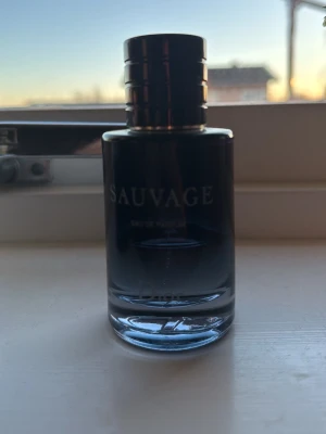 Dior Sauvage Eau de Parfum typ 40-35% kvar - Dior Sauvage Eau de Parfum i en stilren, mörkblå glasflaska med svart lock. Flaskan har en elegant och modern design med tydlig logotyp framtill. En ikonisk herrdoft som utstrålar fräschör och maskulinitet.