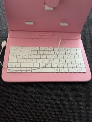 Rosa tangentbord med fodral - Säljer ett portabelt vitt tangentbord med rosa fodral och USB-anslutning. Fodralet är gjort i konstläder och har hållare för surfplatta eller liten laptop. Perfekt för dig som vill ha ett smidigt och snyggt tillbehör till din enhet.