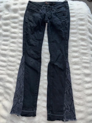 Svarta väldigt lågmidjade bootcut jeans  - Unika svarta jeans från Mogul (?) som jag har sytt om med symaskin till bootcut med ormskinn mönster där nere. De är väldigt lågmidjade (se dragkedjan). Passar storlek 27/32. Rätt bra skick men notera att jag sytt själv ! Har ett litet hål på knät som ska vara där