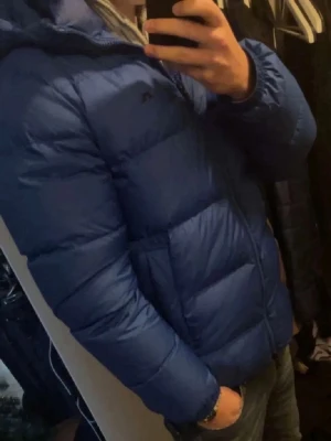 J Lindeberg  - Snygg blå dunjacka från JLindeberg med hög krage och quiltad design. Jackan har dragkedja framtill och diskret logga på bröstet. Perfekt för kalla vinterdagar och riktigt skön att bära. Ny pris ca 6000kr💰Mitt pris 1799💸🔥 Hör gärna av dig om du har någon minsta fråga, jag svarar snabbt🙌🔥🔥