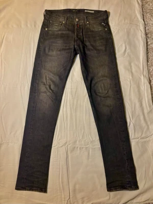 Mörkgrå Replay straight fit - Snygga mörkblå jeans från Replay med klassisk femficksdesign och smal passform. Jeansen har subtila slitningar och en liten röd Replay på bakfickan. Perfekta för en stilren och avslappnad look.