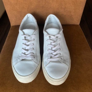  Philippe Model - Säljer ett par klassiska vita sneakers från Philippe Model. Skorna har rund tå, platt sula och är helt i vitt skinn med vita snören. Perfekta för en clean och stilren look.