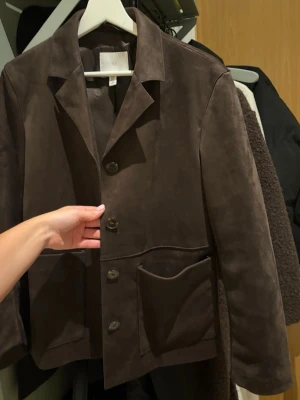 Mörkbrun mocka jacka - Snygg mörkbrun jacka i mocka med krage och  knappar framtill. Använd 1 gång. 