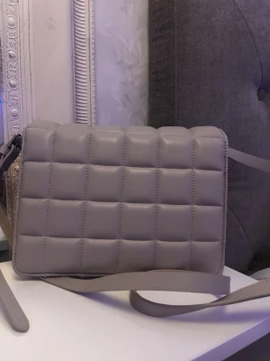 Beige axelväska  - Fin beige väska från H&M!! Använd några gånger och en liten missfärgning (Men inget man tänker på!!knappt syns! Den har en magnet som håller väskan stängd och en axelrem som går att ta av. 