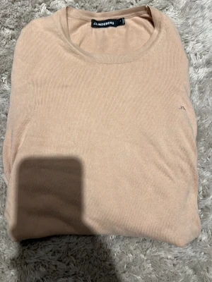 Beige tröja från J.Lindeberg - Snygg beige tröja från J.Lindeberg i klassisk modell med rund hals. Tröjan är enkel och stilren med diskret logga på bröstet. Perfekt för dig som gillar minimalistisk stil och mjuka färger.