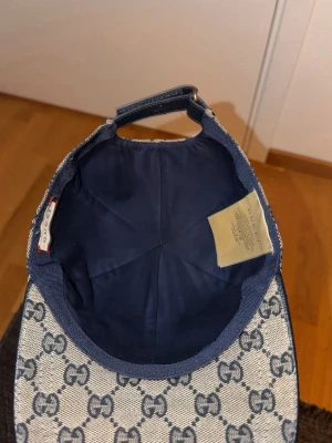 Gucci keps med GG-mönster - Snygg keps från Gucci i beige och marinblått med klassiskt GG-monogram över hela kepsen. Kepsen har en böjd skärm och justerbar rem baktill samt en röd och marinblå rand på sidan. Tillverkad i canvasmaterial med tygfoder inuti. Använt en vecka du får även en box me dig men utan box 1000